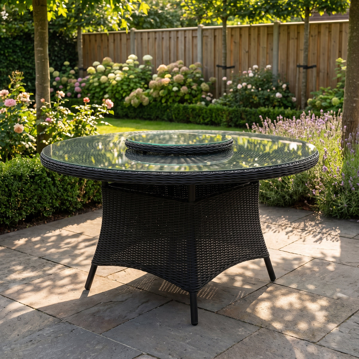 Rio Runder Gartentisch 130 cm mit Glasplatte und fast schwarzem Geflecht in Rock Grey in einem stimmungsvollen Garten - Outnest Gartenmöbel
