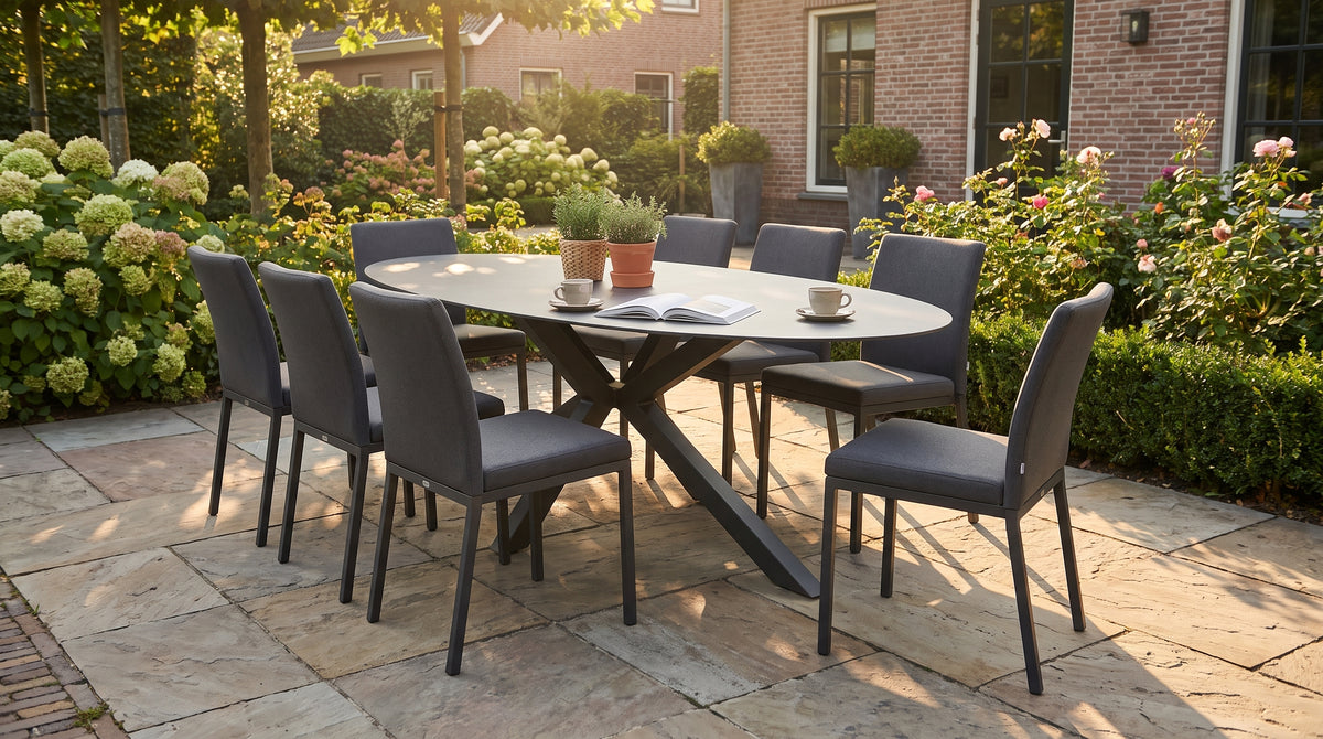 Ovale tuintafel bij zonsondergang, gedekt met koffiekopjes en een boek op een terras